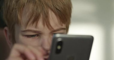 Ciddi Çocuk Akıllı Telefona İsteyerek ve Özenli Bakıyor. Çocuk Arıyor ve Akıllı Telefon Oynuyor. 4K Ağır çekim 10-bit