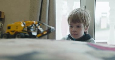 Küçük Çocuk Uzaktan Kumanda 'da Oyuncak Kazıcı' yı oynuyor. Evde Yatakta Oynayan Çocuk. 4K 10-bit