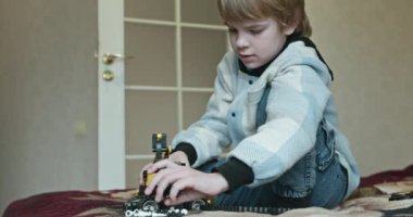 Küçük Çocuk Uzaktan Kumanda 'da Oyuncak Kazıcı' yı oynuyor. Evde Yatakta Oynayan Çocuk. 4K 10-bit