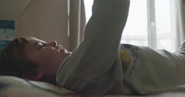 小男孩在家里带着哑铃做运动 孩子做运动躺在床上 4K慢动作60 Fps 10位 — 图库视频影像