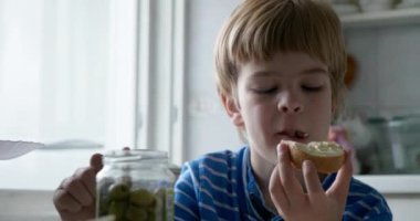 Çocuk evdeki mutfakta tereyağlı ve yeşil zeytinli ekmek yiyor. 4K 10-bit