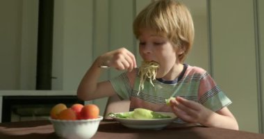 Tatlı çocuk kahvaltıda salatalık ve vejetaryen yemeğiyle spagetti yiyor. Yavaş çekim 60 fps 4K 10-bit