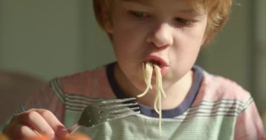 Tatlı çocuk kahvaltıda salatalık ve vejetaryen yemeğiyle spagetti yiyor. Yavaş çekim 60 fps 4K 10-bit