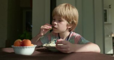 Tatlı çocuk kahvaltıda salatalık ve vejetaryen yemeğiyle spagetti yiyor. Yavaş çekim 60 fps 4K 10-bit