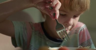 Tatlı çocuk kahvaltıda salatalık ve vejetaryen yemeğiyle spagetti yiyor. Yavaş çekim 60 fps 4K 10-bit