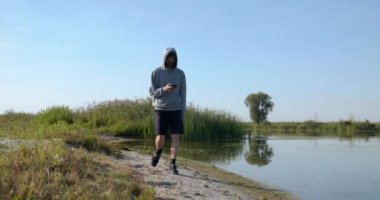 Kafkas Adam Akıllı Telefonla Nehir kenarında Yürüyor. Doğa yürüyüşü. Yavaş çekim 60fps 4K 10-bit