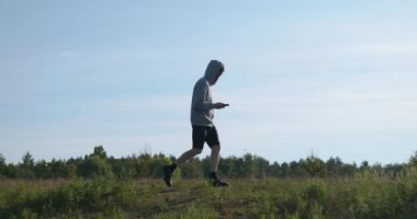 Kafkas Adam Akıllı Telefonla Nehir kenarında Yürüyor. Doğa yürüyüşü. Yavaş çekim 60fps 4K 10-bit