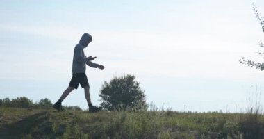 Kafkas Adam Akıllı Telefonla Nehir kenarında Yürüyor. Doğa yürüyüşü. Yavaş çekim 60fps 4K 10-bit