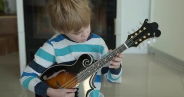 Beyaz çocuk evde Mandolin oynuyor. Avrupalı Çocuk Müzik Çalışması 4K 10-bit