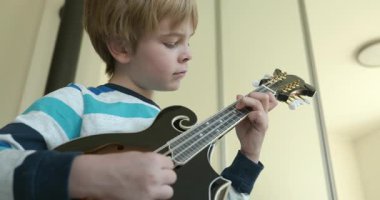 Beyaz çocuk evde Mandolin oynuyor. Avrupalı Çocuk Müzik Çalışması 4K 10-bit