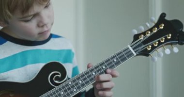 Beyaz çocuk evde Mandolin oynuyor. Avrupalı Çocuk Müzik Çalışması 4K 10-bit