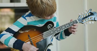 Beyaz çocuk evde Mandolin oynuyor. Avrupalı Çocuk Müzik Çalışması 4K 10-bit