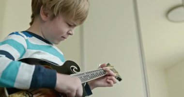 Beyaz çocuk evde Mandolin oynuyor. Avrupalı Çocuk Müzik Çalışması 4K 10-bit