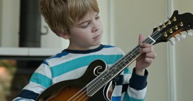 Beyaz çocuk evde Mandolin oynuyor. Avrupalı Çocuk Müzik Çalışması 4K 10-bit