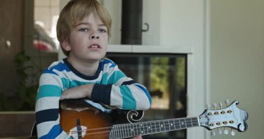 Beyaz çocuk evde Mandolin oynuyor. Avrupalı Çocuk Müzik Çalışması 4K 10-bit