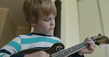 Beyaz çocuk evde Mandolin oynuyor. Avrupalı Çocuk Müzik Çalışması 4K 10-bit