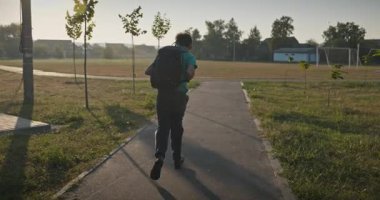 Sırt çantalı çocuk futbol sahasında koşuyor. 4K 10-bit