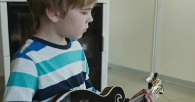 Beyaz çocuk evde Mandolin oynuyor. Avrupalı Çocuk Müzik Çalışması 4K 10-bit