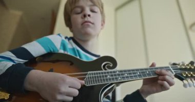 Beyaz çocuk evde Mandolin oynuyor. Avrupalı Çocuk Müzik Çalışması 4K 10-bit