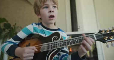 Beyaz çocuk evde Mandolin oynuyor. Avrupalı Çocuk Müzik Çalışması 4K 10-bit