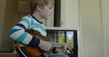 Beyaz çocuk evde Mandolin oynuyor. Avrupalı Çocuk Müzik Çalışması 4K 10-bit