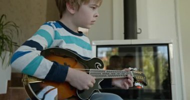 Beyaz çocuk evde Mandolin oynuyor. Avrupalı Çocuk Müzik Çalışması 4K 10-bit