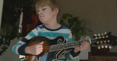 Beyaz çocuk evde Mandolin oynuyor. Avrupalı Çocuk Müzik Çalışması 4K 10-bit