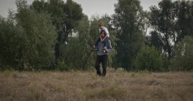 Mutlu Adam, çocuğu omuzlarında taşıyor. Baba ve Çocuk Doğa 4K 10-bit 'te Birlikte Zaman Geçiriyorlar