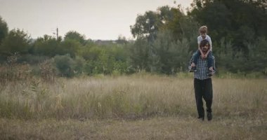 Mutlu Adam, çocuğu omuzlarında taşıyor. Baba ve Çocuk Doğa 4K 10-bit 'te Birlikte Zaman Geçiriyorlar