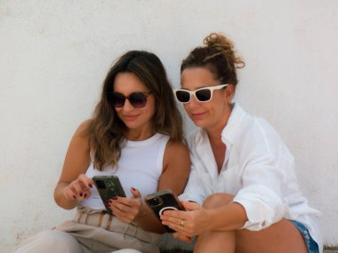 İki kız oturmuş cep telefonlarını izliyorlar.