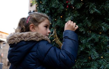 6 yaşında sarışın bir kız, sokakta Noel ışıklarıyla oynuyor.