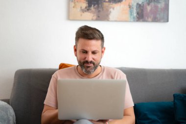 Evdeki kanepede bilgisayarla çalışan çok ciddi bir çocuk.