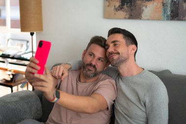 Birkaç Igtbi çocuğu evlerindeki kanepede mutlu bir şekilde oturup pembe cep telefonlarıyla selfie çekiyorlar.