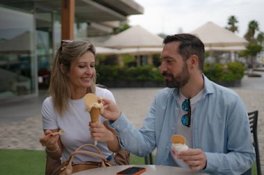 Dondurmayı paylaşan, kafede bir masada oturan gülümseyen bir çift.