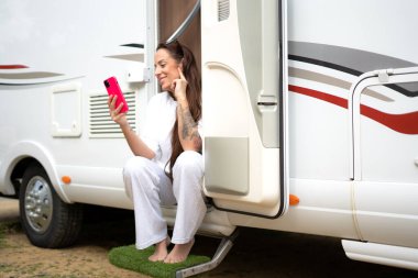 Karavan kapısında oturan kadın elinde telefonla gülümsüyor.