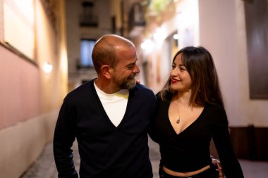 Çiftler gece şehirde yürürken birbirlerine sarılıyorlar.