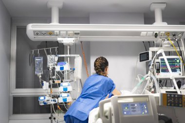 Yoğun bakım ünitesindeki hastayla ilgilenen hemşire, tıbbi ekipmanları ve hayati belirtileri kontrol ediyor.