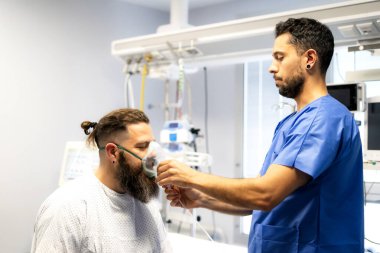 Hastane odasında yüzüne oksijen maskesi takarak hastaya yardım eden hemşire.