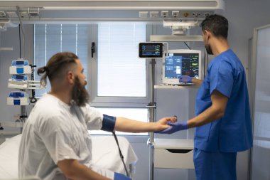 Erkek hemşire hastanın nabzını ölçüyor ve hastane odasında hayati belirtileri kontrol ediyor.