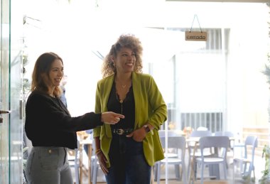 İki iş kadını iş yemeğinden sonra restorandan ayrılıyorlar. Restoran tabelasında Cerrado yazıyor.)