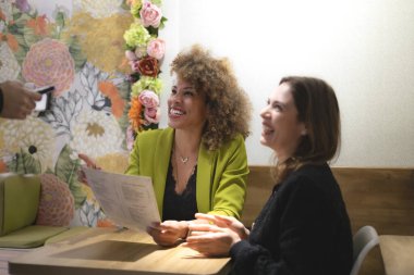 İki kadın temassız kredi kartıyla ödeme yapıyor, elinde menü ve gülümsüyor, restoranda, çiçeklerle.