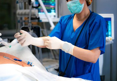 Hemşire, hastayı ameliyathanede ameliyata hazırlarken steril eldiven takıyor.