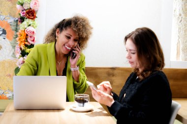 İki iş kadını bir kafede birlikte çalışıyorlar. Laptop ve akıllı telefon kullanıyorlar.