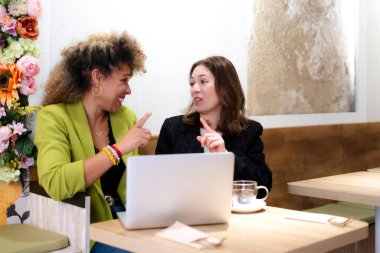 İki iş kadını kafeteryada gayri resmi toplantı yaparken dizüstü bilgisayarı işaret ediyor.