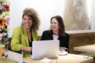 İki neşeli iş kadını, bir kafede verimli bir toplantının keyfini çıkarırken aynı anda bir dizüstü bilgisayarla gülüyorlar.