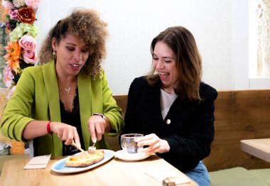 İki iş kadını birlikte hafif bir öğle yemeğinin tadını çıkarıyor. Sıcak bir kafede gülüyor ve sohbet ediyorlar.