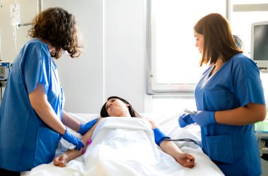 Hastane yatağında yatan bir kadın hastayla ilgilenen iki hemşire hayati belirtileri kontrol ediyor ve tıbbi yardım sağlıyor.