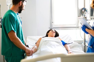Doktor bir hastanın elini tutuyor, bir hastane odasında onu rahatlatıyor.