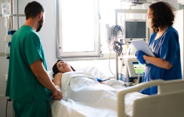 Doktorlar ve hemşireler hastane yatağında yatan bir kadın hastaya tıbbi bakım sağlıyorlar.