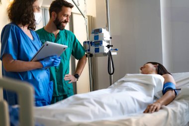 Doktorlar hastane yatağında dinlenen kadın hastalara bakarken tıbbi kayıtları inceliyor.